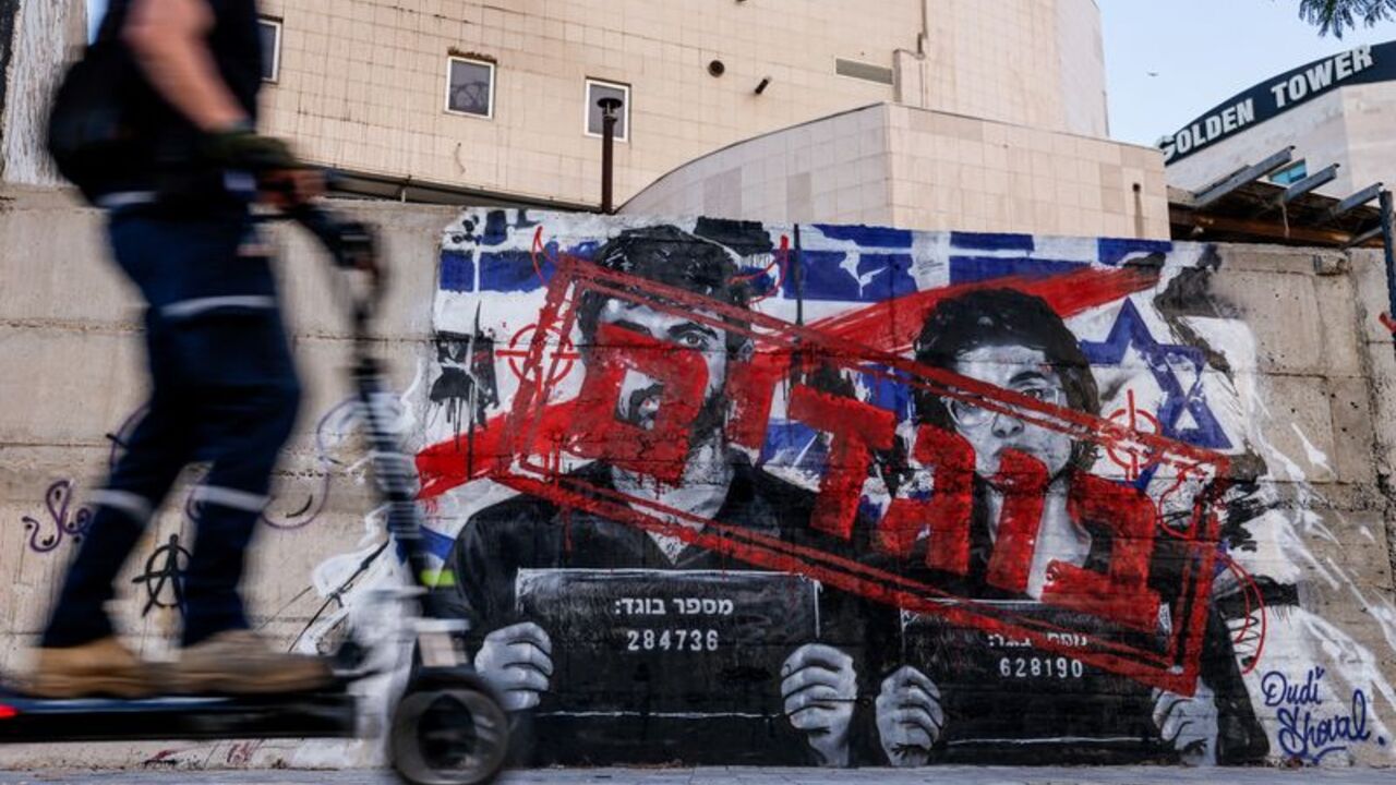 A man rides a scooter as he passes graffiti depicting Yuval Abraham and Rachel Szor, the directors of the documentary film NAZA, and the word "traitors" in Hebrew, on a wall in Ashdod
