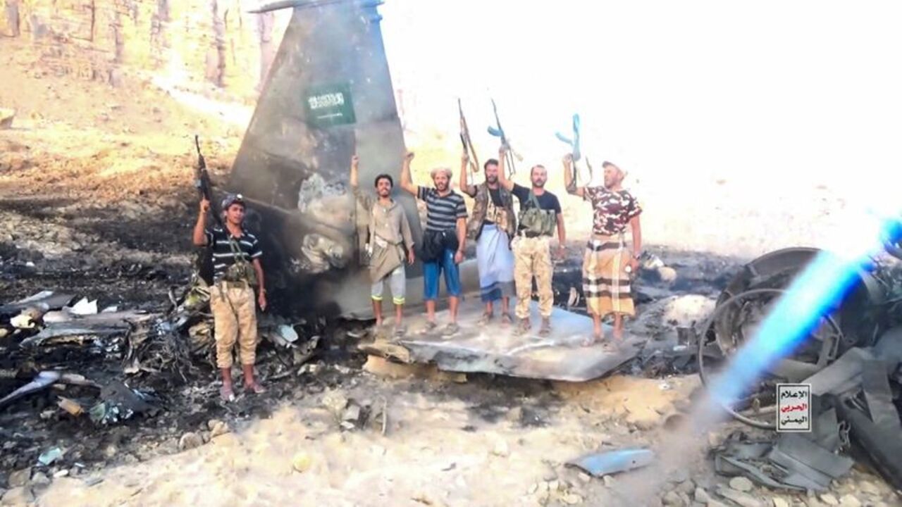 Houthi fighters stand in front of what they say is a downed Saudi jet, at a location given as Yemen