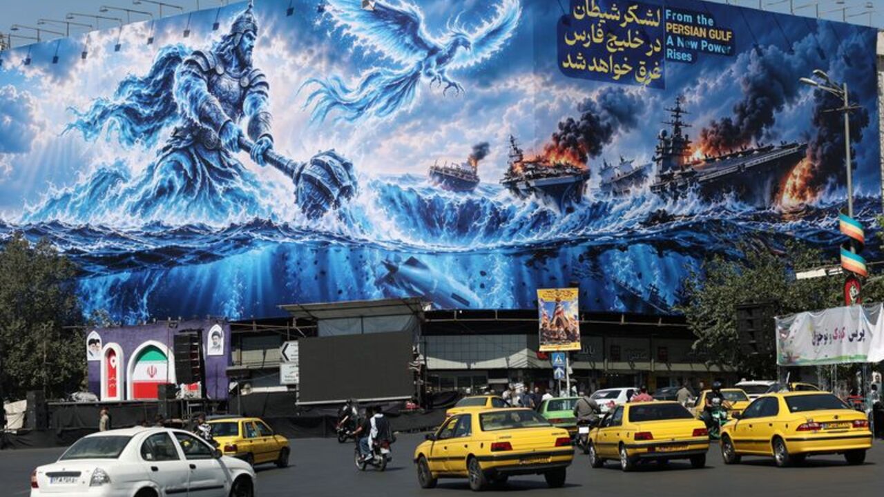 People drive past a billboard about the Strait of Hormuz, on a building in Tehran
