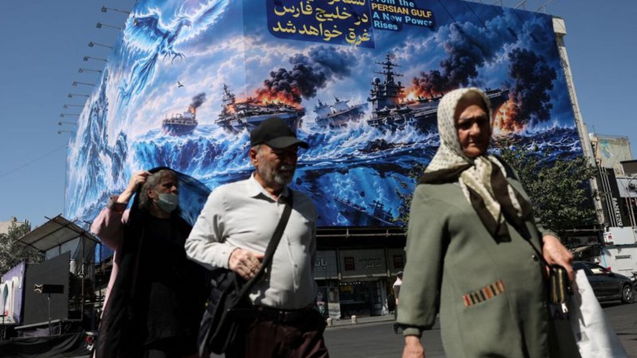 FILE PHOTO: People walk past a billboard about the Strait of Hormuz, on a building in Tehran