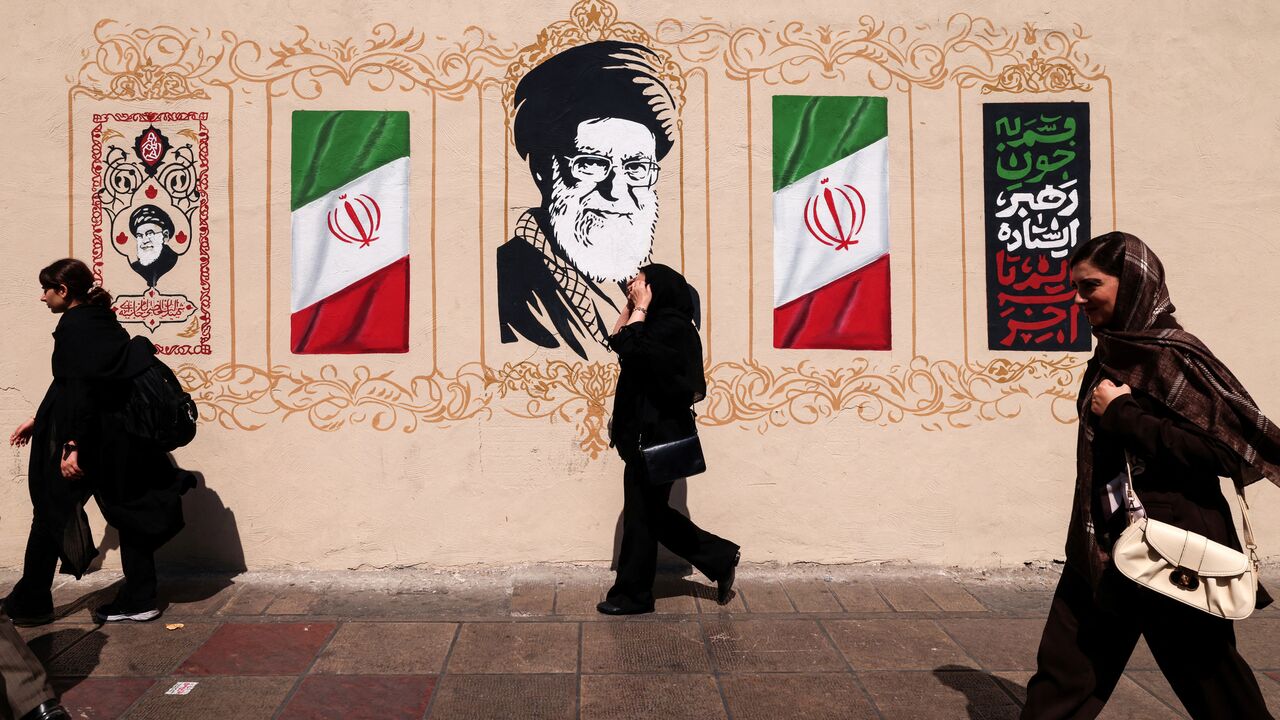 Iranians walk past a wall decorated with the image of assassinated Iranian supreme leader Ayatollah Ali Khamenei and the national flag, in central of Tehran on Sept. 14, 2026.  
