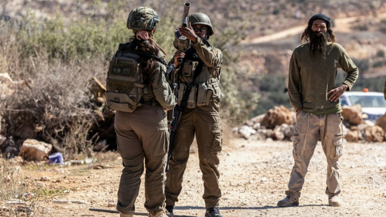 Israeli soldiers and an Israeli settler gather on a road close to an olive grove following a reported attack by settlers on a Palestinian home in the Israeli-occupied West Bank village of Turmus Ayya