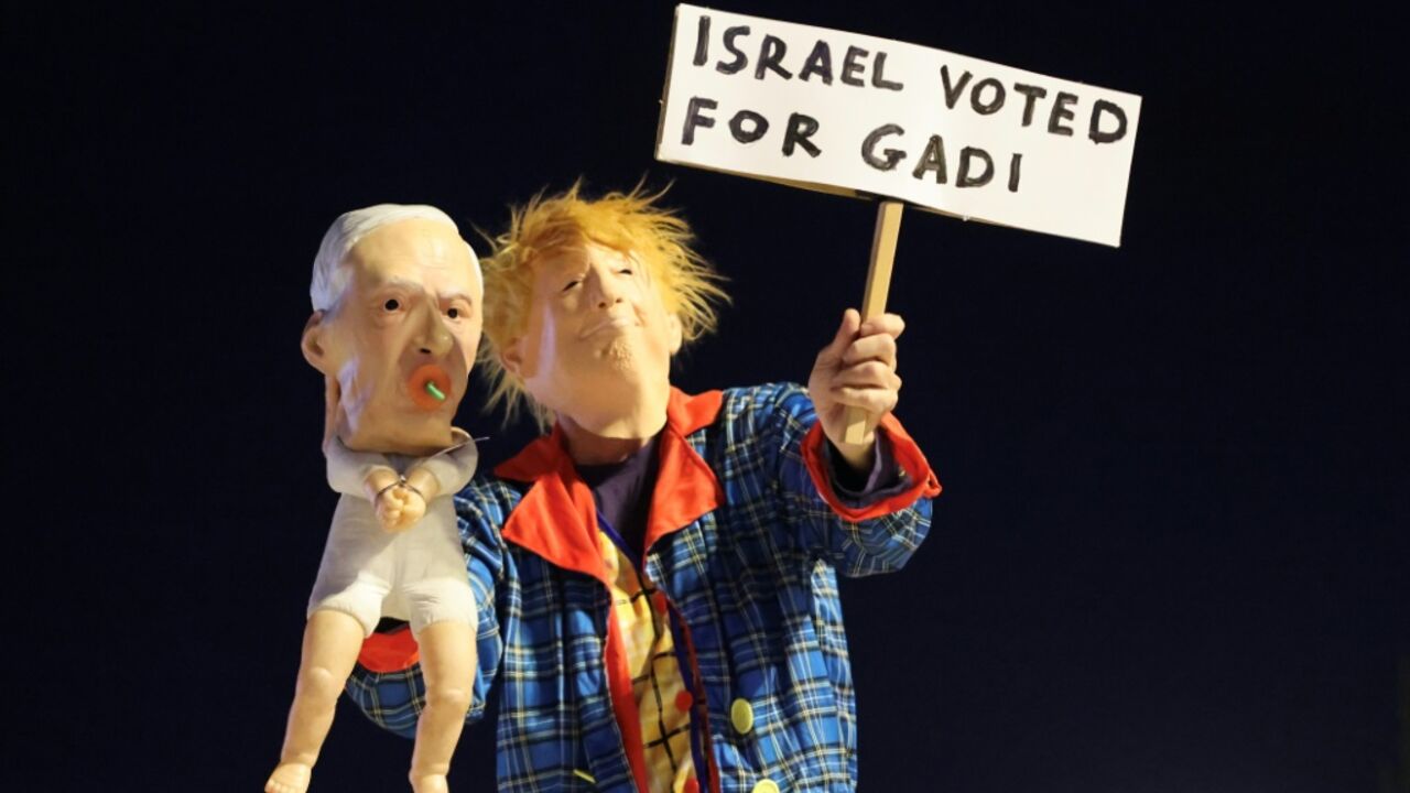 A protester in Tel Aviv dressed as US President Donald Trump holds a puppet depicting Israeli Prime Minister Benjamin Netanyahu, with a sign supporting opposition leader Gadi Eisenkot