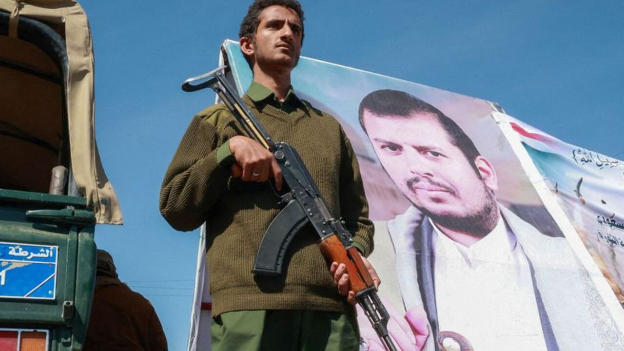 Member of Houthi security forces stands next to a poster of Houthi leader Abdul-Malik al-Houthi in Sanaa