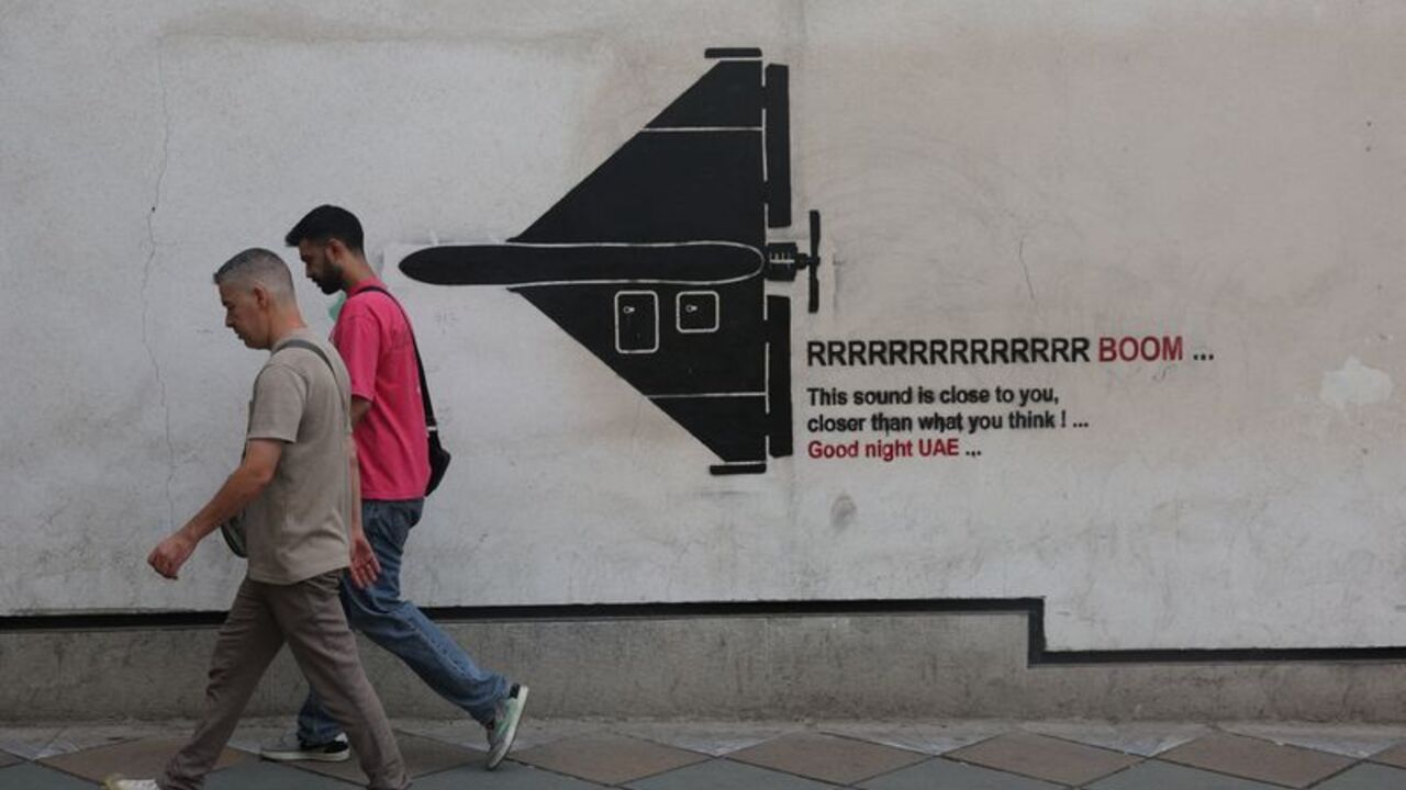 People walk past a mural depicting an Iranian drone on a street in Tehran