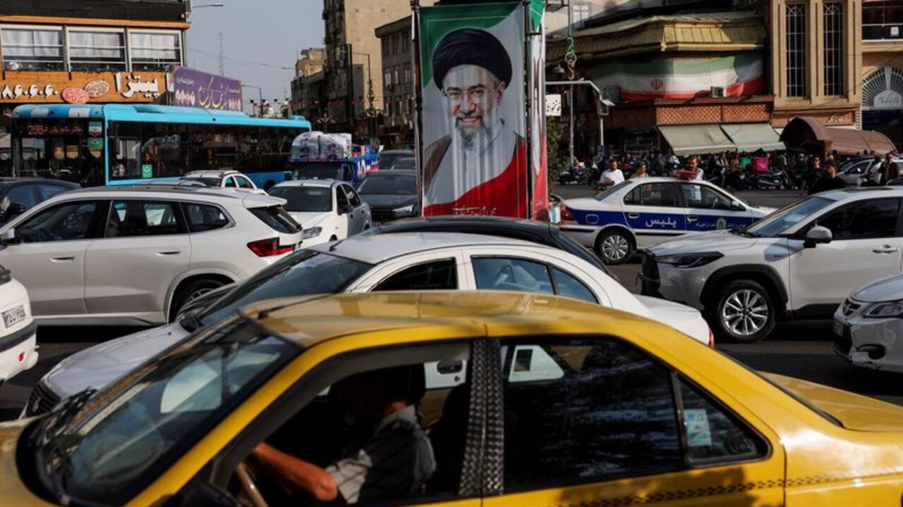 People drive next to a banner with a picture of Iran's Supreme Leader Mojtaba Khamenei, on a street in Tehran