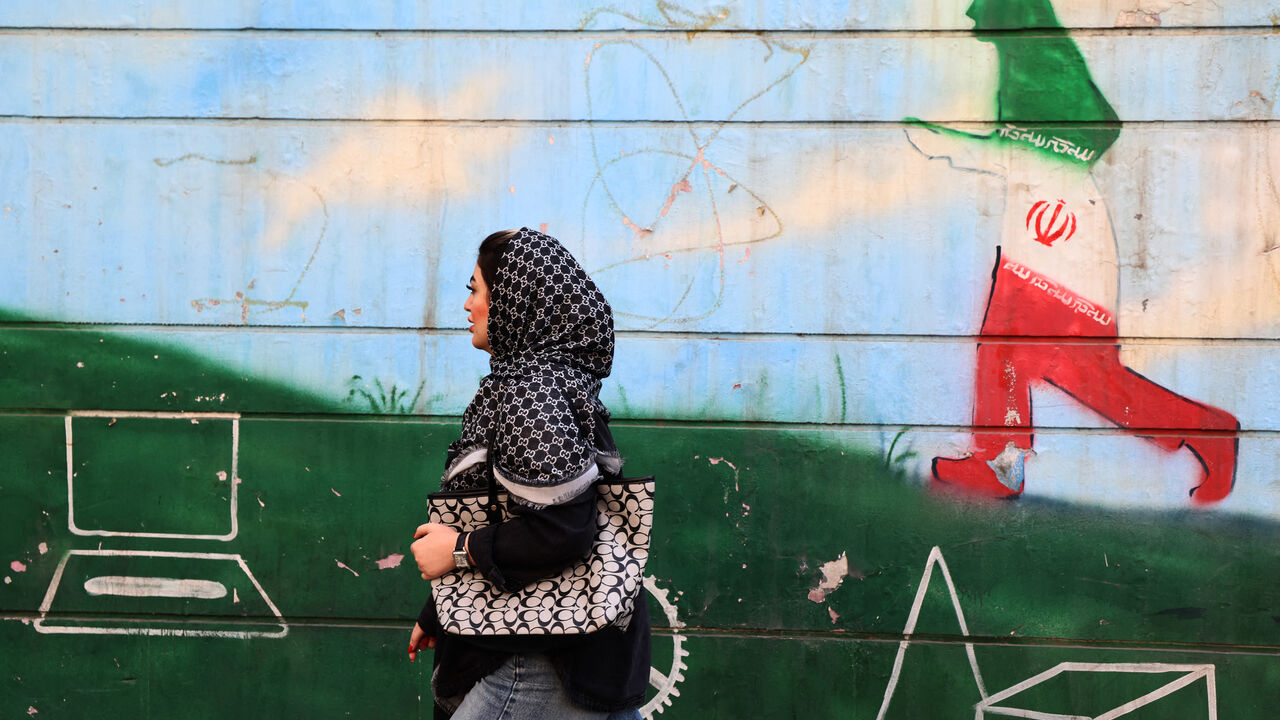 A woman walks past a wall painting in the colours of the Iranian flag in Tehran on February 25, 2026. (Photo by ATTA KENARE / AFP via Getty Images)