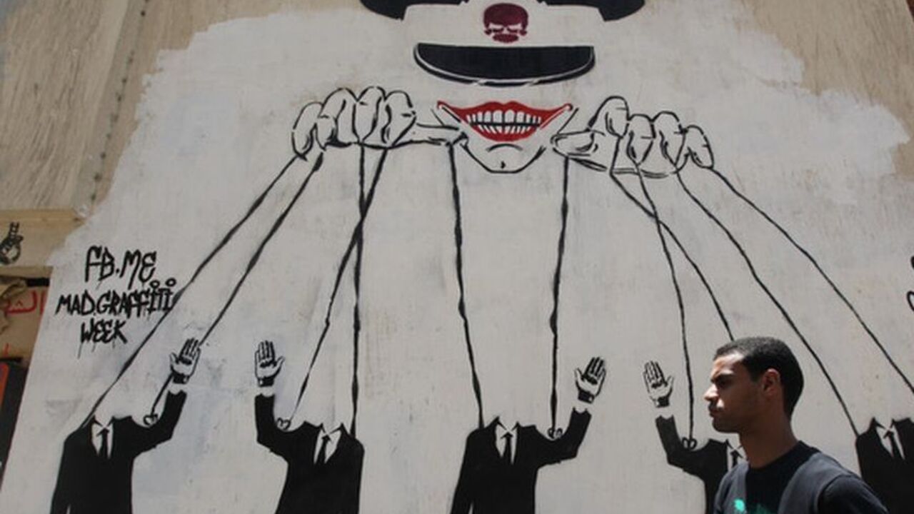 An Egyptian man walks in front of a wall sprayed with graffiti, depicting  the ruling military council controlling the presidential elections as a puppet show, near Tahrir Square in downtown Cairo May 16, 2012. Voting starts in Egypt's presidential election on May 23-24 to choose who will succeed Hosni Mubarak, who was swept from office last year in a popular uprising. REUTERS/Amr Abdallah Dalsh  (EGYPT - Tags: POLITICS CIVIL UNREST ELECTIONS TPX IMAGES OF THE DAY)