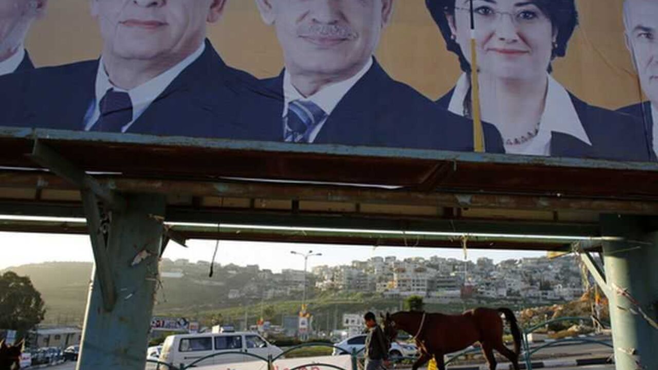 A man walks with a horse near a campaign poster for the National Democratic Assembly party in the Israeli-Arab city of Umm el-Fahm January 14, 2013. Disillusioned, disappointed and divided, Israeli Arab voters will traipse to the polls next week in ever dwindling numbers, aware that none of their community will have any say in how the country is run. Picture taken January 14, 2013. REUTERS/Ammar Awad (ISRAEL - Tags: POLITICS ELECTIONS ANIMALS)