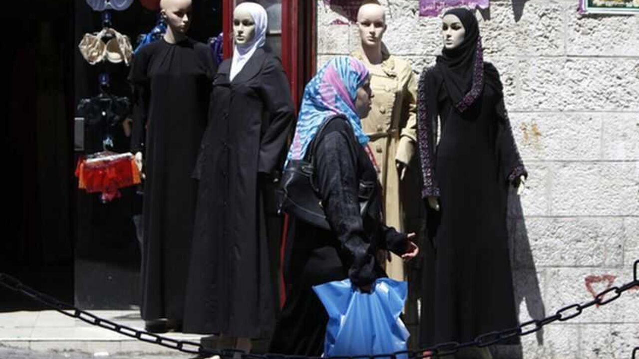 A Palestinian woman walks past a clothing store in the West Bank city of Ramallah September 4, 2012. Palestinian dreams of building a powerful economy to speed their drive towards independence could soon be plunged into darkness. The cash-strapped government of the occupied West Bank, the Palestinian Authority, is so behind with its bills that an Israeli electricity supplier has threatened to cut the power unless they pay outstanding debt of almost $80 million. Picture taken September 4, 2012. To match Feat