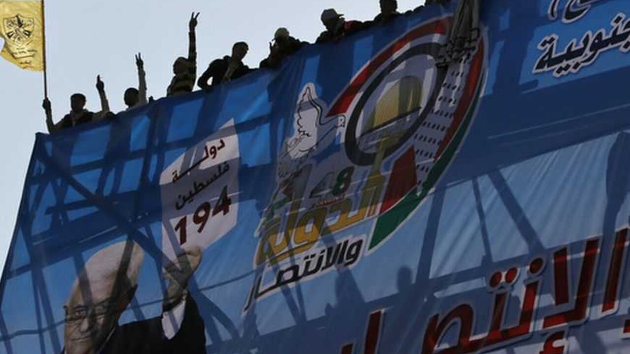 Palestinians stand behind a poster depicting Palestinian President Mahmoud Abbas during a rally marking the 48th anniversary of the founding of the Fatah movement, in Gaza City January 4, 2013. Hundreds of thousands of Palestinians joined a rare rally staged by President Mahmoud Abbas's Fatah group in Gaza on Friday, as tensions ease with rival Hamas Islamists ruling the enclave since 2007. REUTERS/Suhaib Salem (GAZA - Tags: POLITICS ANNIVERSARY) - RTR3C3JJ
