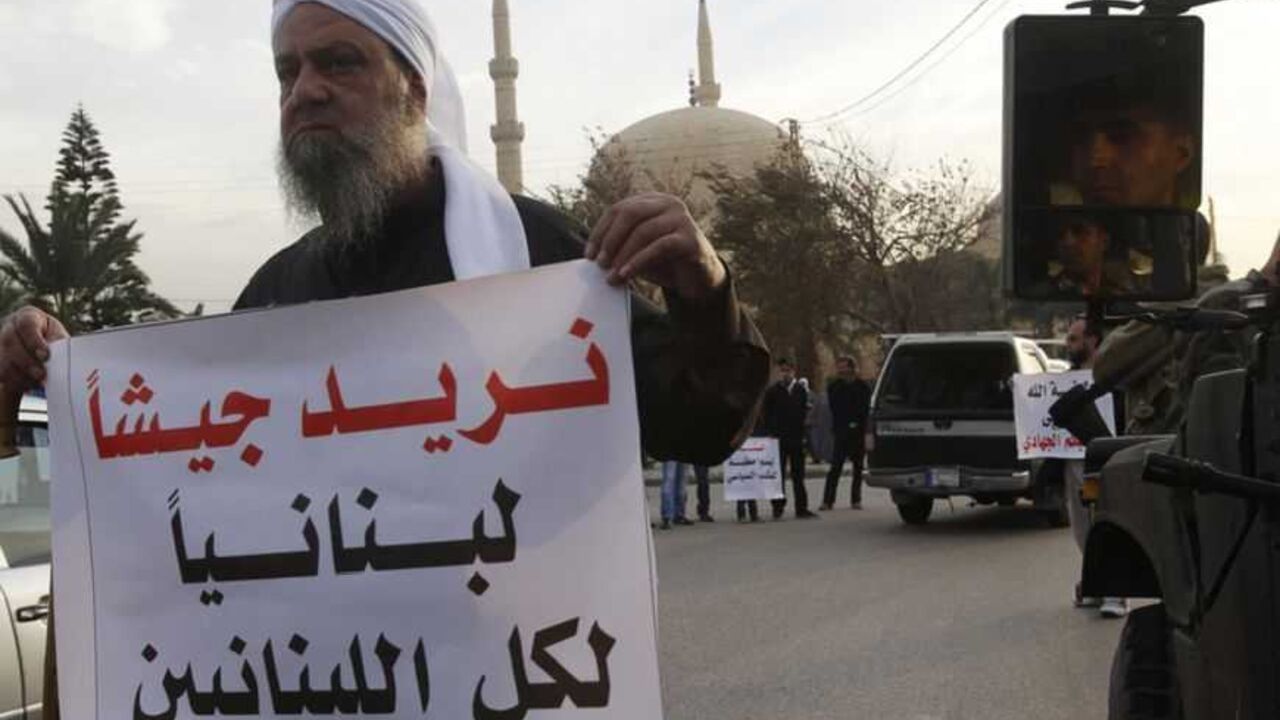 A supporter of Sunni Muslim Salafist leader Ahmad al-Assir carries a placard as he stands next to Lebanese soldiers on their military vehicle, during a protest in Sidon, southern Lebanon, in support of residents of the northeastern town of Arsal in the country's Bekaa Valley, February 5, 2013. Four Lebanese soldiers and two gunmen were killed in clashes in Bekaa Valley on Friday after militants attacked a Lebanese army unit, security sources said. The placard reads: "We want a Lebanese Army for all Lebanese