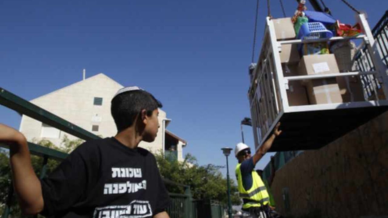 A boy watches as a crane lowers the belongings of families moving out of the Ulpana neighbourhood of the Beit El settlement June 26, 2012. Settlers on Tuesday began moving out of apartment blocs that Israel's Supreme Court ruled had been built illegally on Palestinian-owned land, after reaching an agreement with the government to go quietly. His  T-shirt reads, "Ulpana neighbourhood, will return".  REUTERS/Baz Ratner (WEST BANK - Tags: POLITICS RELIGION) - RTR3463H