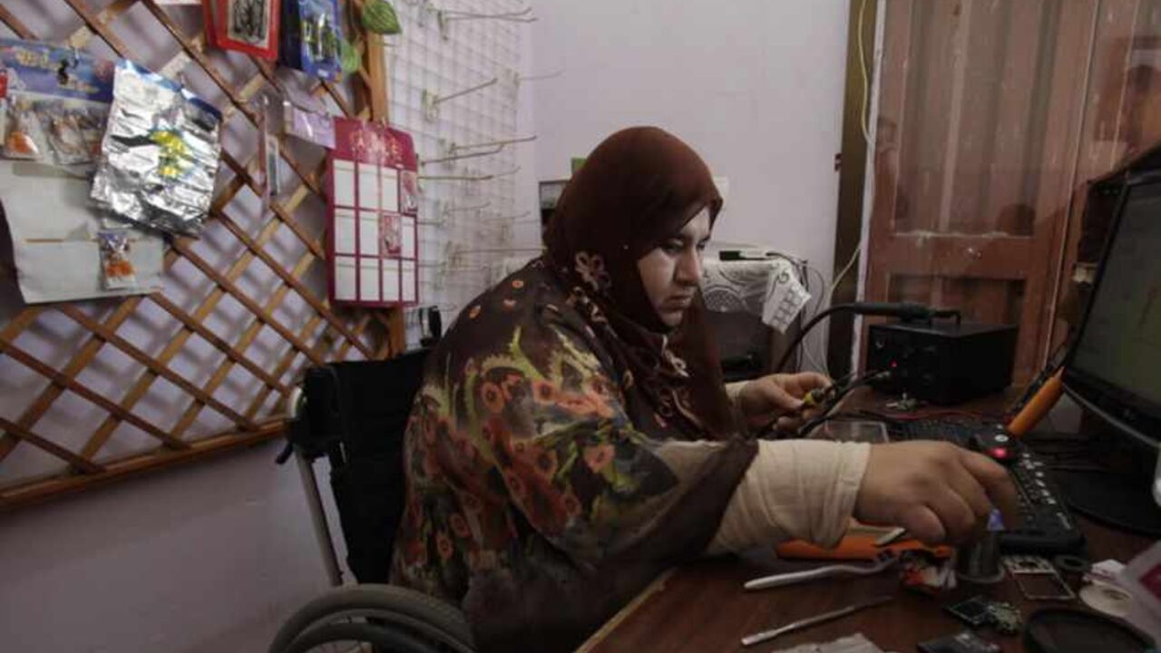 A wheelchair-bound Palestinian woman Manal al-Satari, 37, fixes cell phones at her shop in Rafah in the southern Gaza Strip April 7, 2013. 
REUTERS/Ibraheem Abu Mustafa (GAZA - Tags: SOCIETY) - RTXYBPS
