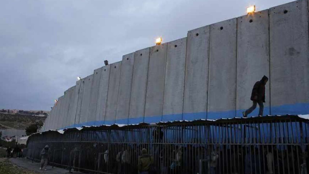Palestinian labourers queue next to a section of the controversial Israeli barrier as they wait to cross into Jerusalem at an Israeli checkpoint in the West Bank town of Bethlehem March 18, 2013. U.S. President Barack Obama is due to make his first official visit to Israel and the Palestinian Territories this week, looking to improve ties after sometimes rocky relations with both sides during his first term in office. Israeli settlement expansion lies at the heart of much of the rancour between Israeli Prim