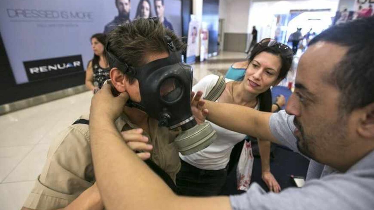 An Israeli Postal Service employee shows a man how to adjust a gas mask at a distribution point at a shopping mall in the West Bank Jewish settlement of Maale Adumim near Jerusalem  August 26, 2013. Thousands of Israelis lined up for gas masks at nationwide distribution centers or phoned in orders fearing a deadly chemical weapons attack in Syria may wind up ensnaring their own nation in conflict, officials and analysts said on Monday. REUTERS/Baz Ratner (WEST BANK - Tags: POLITICS MILITARY CIVIL UNREST) - 