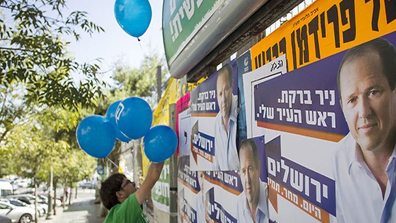 A supporter of the left wing Meretz party campaigning for municipal elections hangs balloons next to campaign posters of Jerusalem Mayor Nir Barkat in Jerusalem October 22, 2013. REUTERS/Baz Ratner (JERUSALEM - Tags: POLITICS ELECTIONS) - RTX14JPY