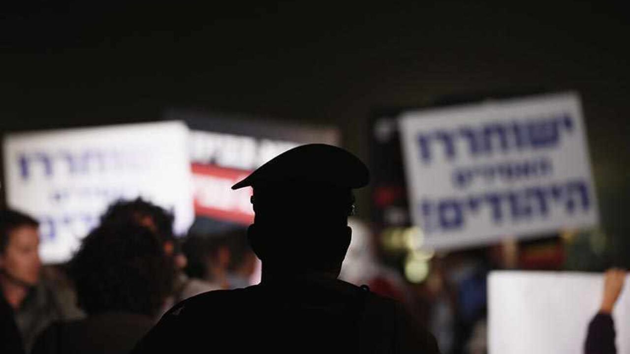 A police officer watches Israeli protesters take part in a rally against the release of Palestinian prisoners in Israeli jails outside Ofer prison near the West Bank city of Ramallah, October 29, 2013. Israel is to release 26 Palestinian prisoners in a second stage of a deal brokered by the United States in July that brought a resumption of peace talks. REUTERS/Darren Whiteside (ISRAEL - Tags: CIVIL UNREST POLITICS RELIGION) - RTX14SWY