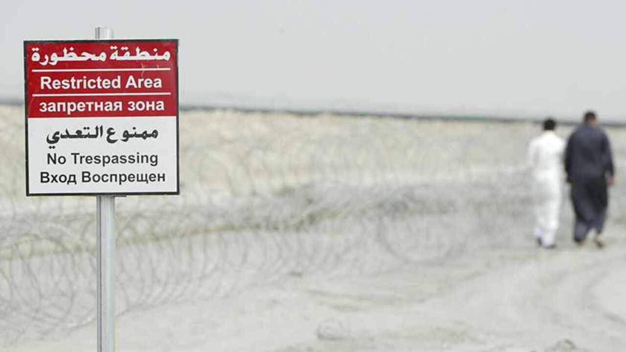 Men walk past a sign in al-Toraba area near an oilfield of West Qurna-2 in Basra, 420 km (261 miles) southeast of Baghdad, October 26, 2013. After struggling for decades from sanctions and wars, most recently the U.S.-led invasion from 2003-2011, expectations run high among the 150,000 tribesmen living on West Qurna-2, the world's second-largest undeveloped oilfield. Their sheer number leaves Lukoil with a far tougher challenge than rival firms operating the huge but sparsely populated fields nearby. Pictur