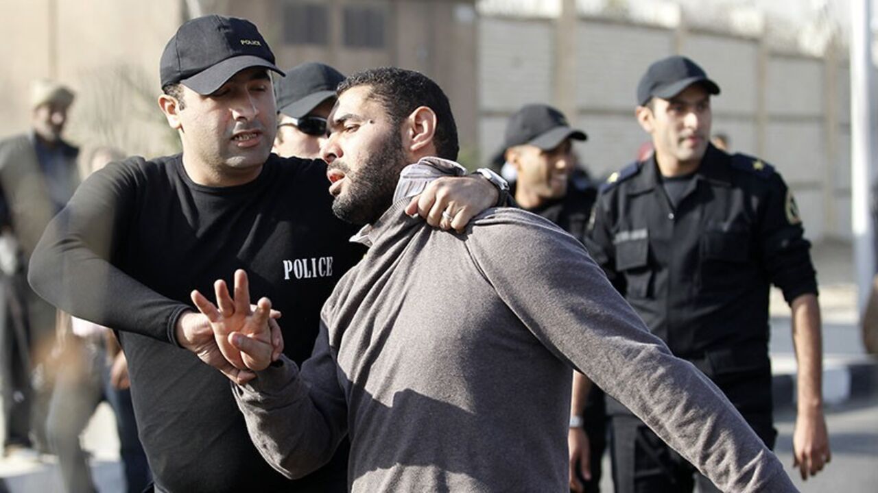 Police and security forces detain a man, supporter of the Muslim Brotherhood and ousted Egyptian President Mohamed Mursi, as he gestures with four fingers outside a police academy where Mursi's second trial session was due to take place, on the outskirts of Cairo January 8, 2014. Mursi's second day in court was held up on Wednesday when bad weather delayed his flight to the Cairo police academy where he was due to face trial for inciting the killing of protesters, state media reported. The four-finger "Raba