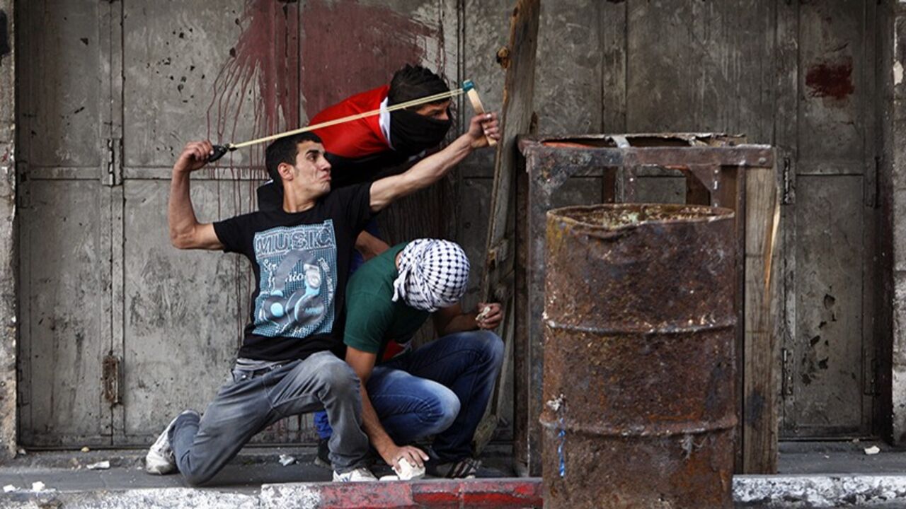 A Palestinian protester uses a sling to hurl a stone at Israeli troops during clashes following a rally to show solidarity with Palestinian prisoners held in Israeli jails, in the West Bank city of Hebron May 16, 2014. Some 120 Palestinians jailed without trial in Israel have been on an open-ended hunger strike, eating only salt and drinking water, for the past 23 days to demand an end to so-called "administrative detention". REUTERS/Mussa Qawasma (WEST BANK - Tags: POLITICS CIVIL UNREST) - RTR3PIGO