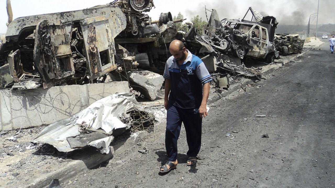 A man walks past near remains of burnt vehicles belonging to Iraqi security forces in the northern Iraq city of Mosul, June 13, 2014. A Sunni Islamist offensive threatening to dismember Iraq seemed to slow on Saturday after days of lightning advances as government forces reported regaining territory in counter-attacks, easing pressure on Baghdad's Shi'ite-led government. Picture taken June 13, 2014. REUTERS/Stringer (IRAQ - Tags: CIVIL UNREST POLITICS) - RTR3TR9S