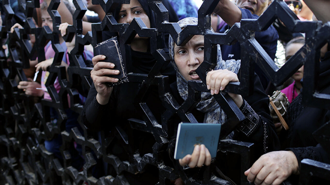 Palestinians standing behind the gate of Rafah crossing hold their passports as they try to cross into Egypt, in the southern Gaza Strip July 10, 2014. At least 74 Palestinians, most of them civilians, have been killed in Israel's Gaza offensive, Palestinian officials said on Thursday, and militants kept up rocket attacks on Tel Aviv and other cities in warfare showing no signs of ending soon. Egypt's state news agency said Egyptian authorities had decided to open the Rafah border crossing to Gaza on Thursd