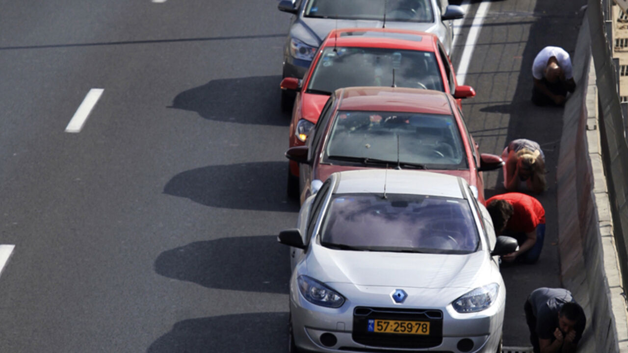 Drivers take cover beside their cars on a highway as an air raid siren, warning of incoming rockets, sounds in Tel Aviv July 9, 2014. Israeli air strikes shook Gaza every few minutes on Wednesday, and militants kept up rocket fire at Israel's heartland in intensifying warfare that Palestinian officials said has killed at least 47 people in the Hamas-dominated enclave. REUTERS/Stringer (ISRAEL - Tags: POLITICS CIVIL UNREST) - RTR3XVPQ
