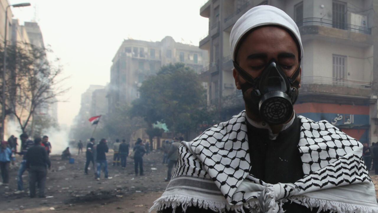An Egyptian cleric who is a protester, prays as protesters run from tear gas fired by riot police during clashes along a road which leads to the Interior Ministry, near Tahrir Square in Cairo November 22, 2011.Egyptians frustrated with military rule battled police in the streets again on Tuesday as the generals scrambled to cope with the cabinet's proffered resignation after bloodshed that has jolted plans for Egypt's first free election in decades. REUTERS/Amr Abdallah Dalsh (EGYPT - Tags: CIVIL UNREST POL