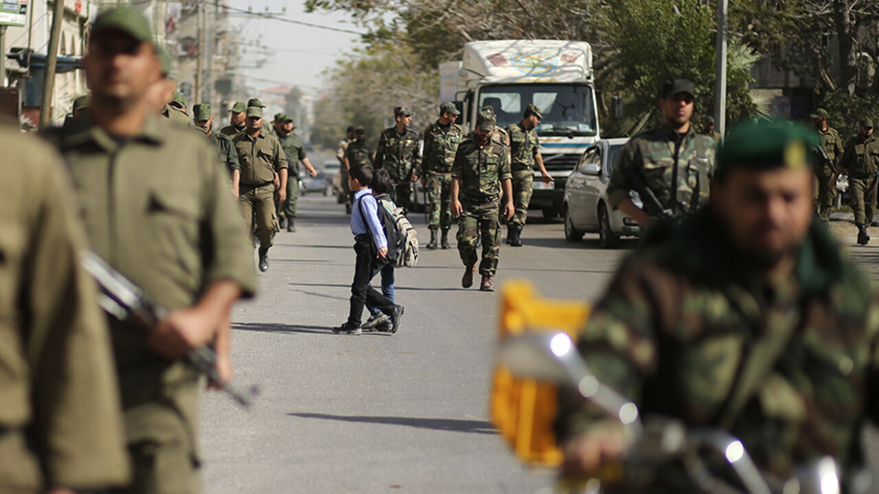 Palestinian students cross the street as members of Palestinian security forces loyal to Hamas march in Gaza City February 10, 2015. 
REUTERS/Mohammed Salem (GAZA - Tags: MILITARY EDUCATION SOCIETY) - RTR4OYIN