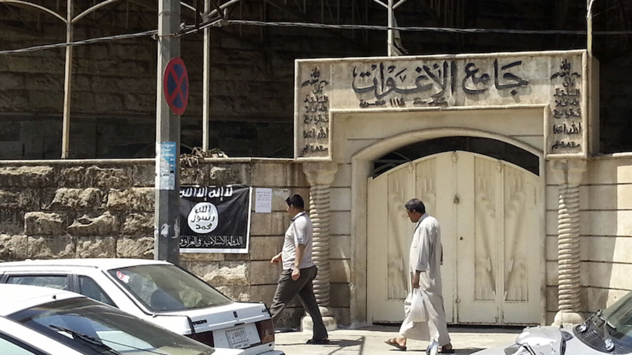 People walk past a banner (in black and white) belonging to the Islamic State in Iraq and the Levant (ISIL) in the city of Mosul, June 28, 2014. Since early June, ISIL militants have overrun most majority Sunni Muslim areas in the north and west of Iraq, capturing the biggest northern city Mosul and late dictator Saddam Hussein's hometown of Tikrit. The banner reads, "There is no God but God, and Mohammad is his messenger."  REUTERS/Stringer (IRAQ - Tags: CIVIL UNREST POLITICS) - RTR3W71S