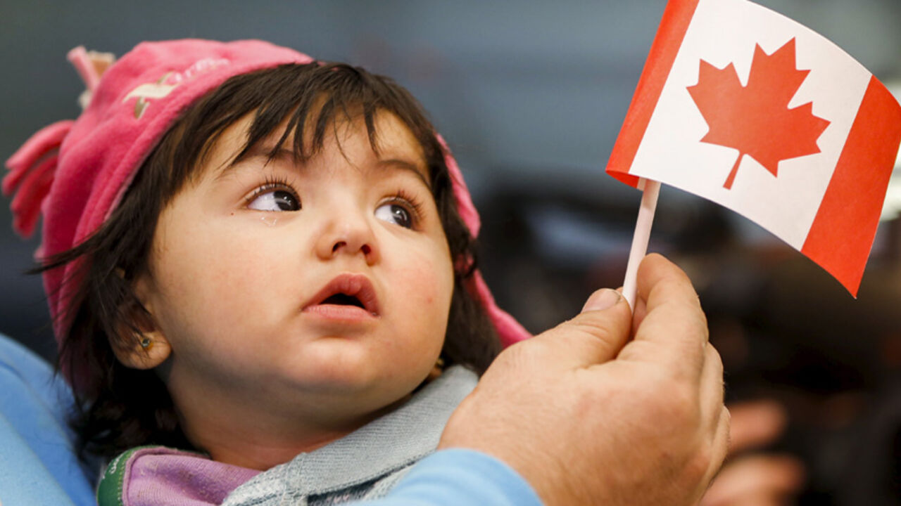 A young Syrian refugee looks up as her father holds her and a Canadian flag at the as they arrive at Pearson Toronto International Airport in Mississauga, Ontario, December 18, 2015.    REUTERS/Mark Blinch       TPX IMAGES OF THE DAY      - RTX1ZBYE