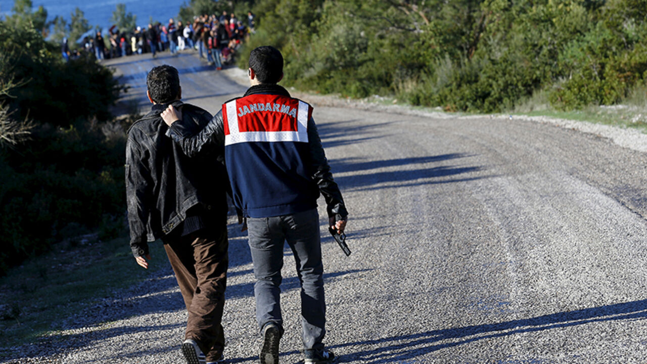 A Turkish Gendarme officer detains a man believed to be a smuggler as Syrian refugees who are prevented from sailing off for the Greek island of Lesbos by dinghies wait in the background near a beach in the western Turkish coastal town of Dikili, Turkey, March 5, 2016. REUTERS/Umit Bektas      TPX IMAGES OF THE DAY      - RTS9EC6