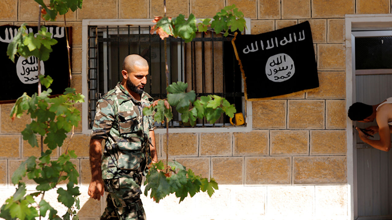 A member of Turkish-backed Free Syrian Army (FSA), seen with the Islamic State flags in the background, walks outside of a building in the border town of Jarablus, Syria, August 31, 2016. REUTERS/Umit Bektas - RTX2NQ7V