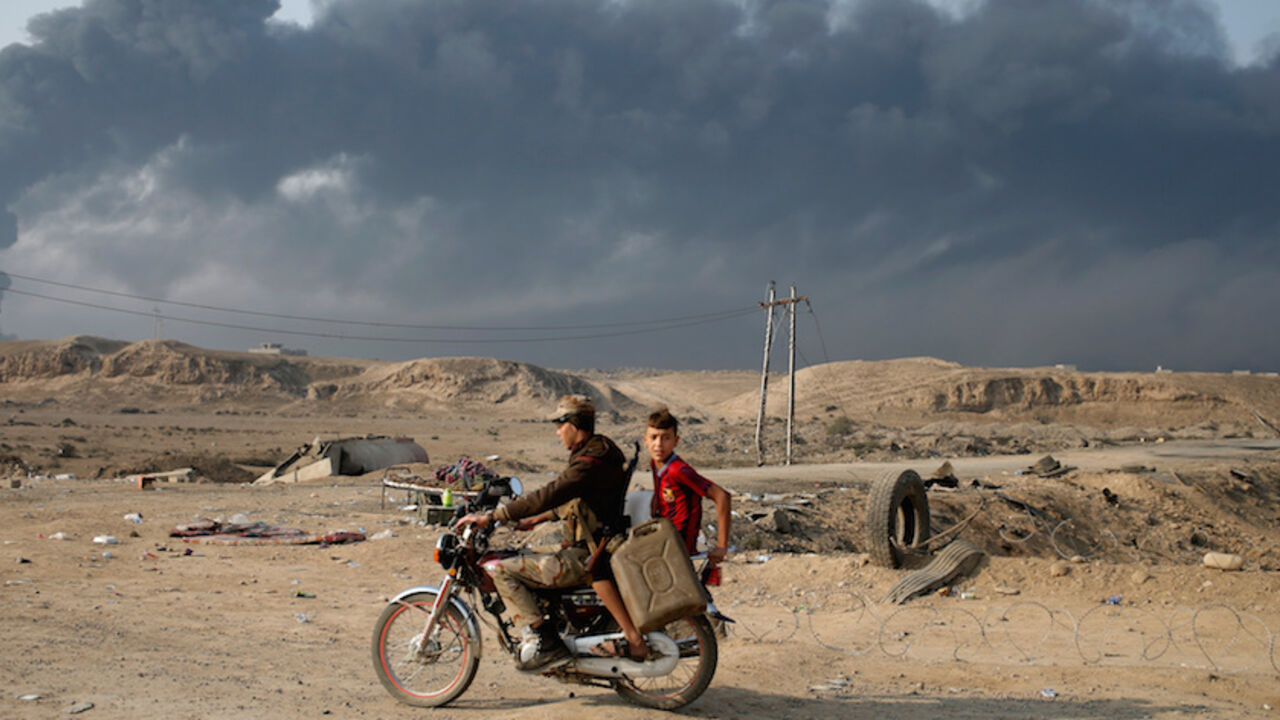 Armed members of Shi'ite militia Hashid Shaabi ride a motorbike near Qayyara, south of Mosul, Iraq October 27, 2016. Smoke in the background is from burning oilfields set ablazed by Islamic State fighters. REUTERS/Goran Tomasevic - RTX2QNPU