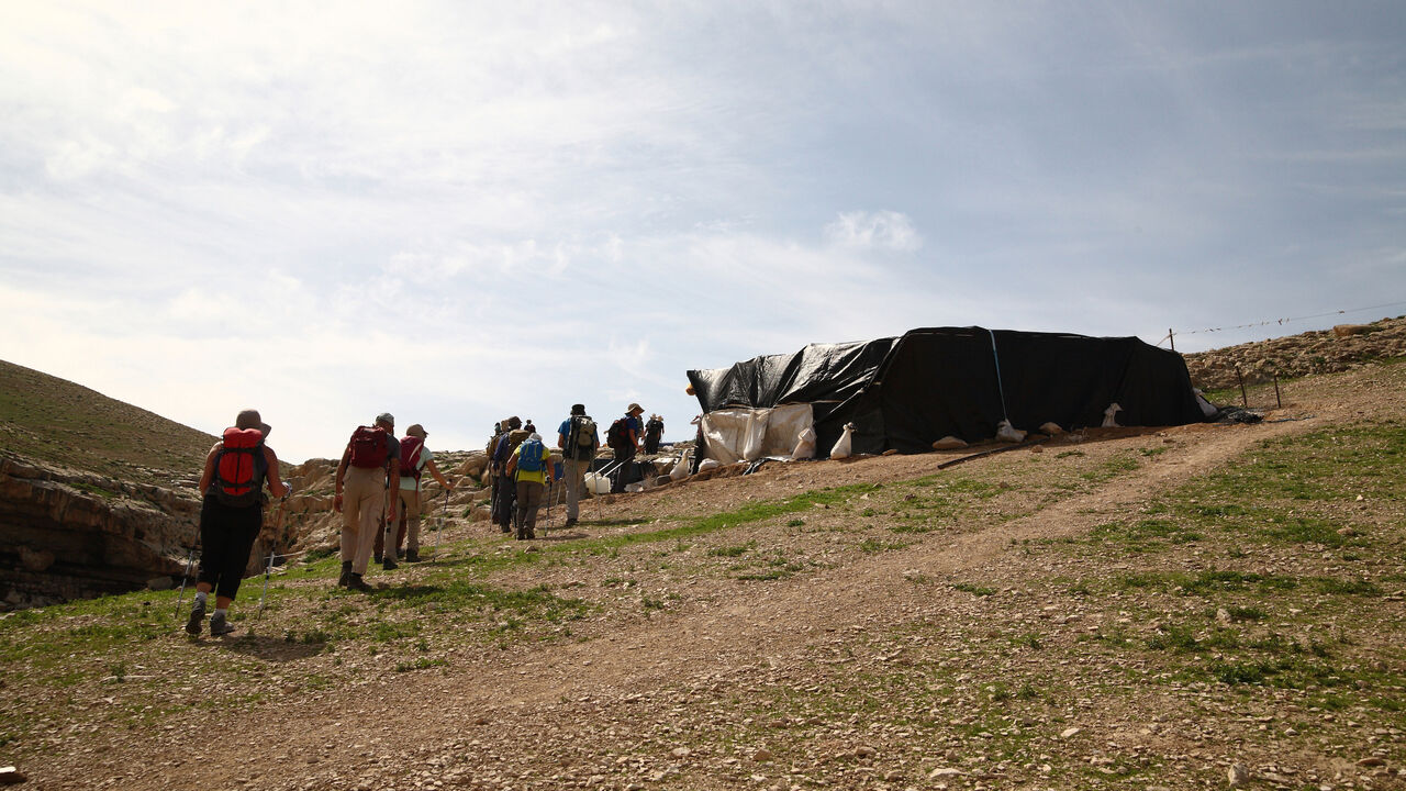 A line of hikers walk towards a semi-permanent, plastic-wrapped structure in a hillside, Bedouin nomad settlement , near Nachal (or Nahal Og), in the Judean Desert, West Bank, Israel, February 13, 2016. . (Photo by Dan Porges/Getty Images)
