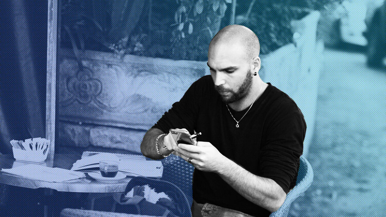 A young man uses his smartphone as he sits at an outdoor table in the Carousela Restaurant (in the Rehavia neighborhood), Jerusalem, Israel, November 18, 2014. (Photo by Dan Porges/Getty Images)