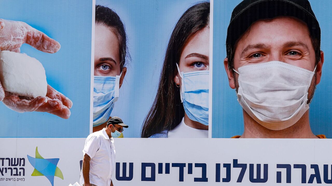 A mask-clad man walks past a billboard showing other mask-clad faces and adequate social distance measures, raising awareness about COVID-19 coronavirus pandemic precautions, in the centre of the Israeli city of Ramat Gan, east of Tel Aviv, on July 17, 2020. - Israel's government said it was imposing new restrictions to limit the spiraling spread of coronavirus in the hope of avoiding a general lockdown further along the line. It said that from 5:00pm local time (1400 GMT) on Friday until 5:00am every Sunda