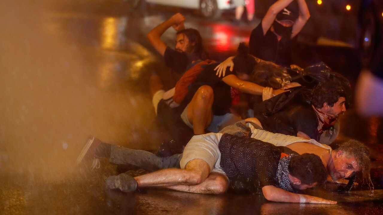 TOPSHOT - Protesters crouch down as Israeli police use water cannons during clashes at a demonstration against the Israeli prime minister outside his official residence in Jerusalem, early on July 22, 2020. - Israeli Prime Minister Benjamin Netanyahu, 70, was indicted in January for bribery, fraud and breach of trust in three cases. He denies all the charges and accuses the media and legal officials of a witch hunt. (Photo by AHMAD GHARABLI / AFP) (Photo by AHMAD GHARABLI/AFP via Getty Images)