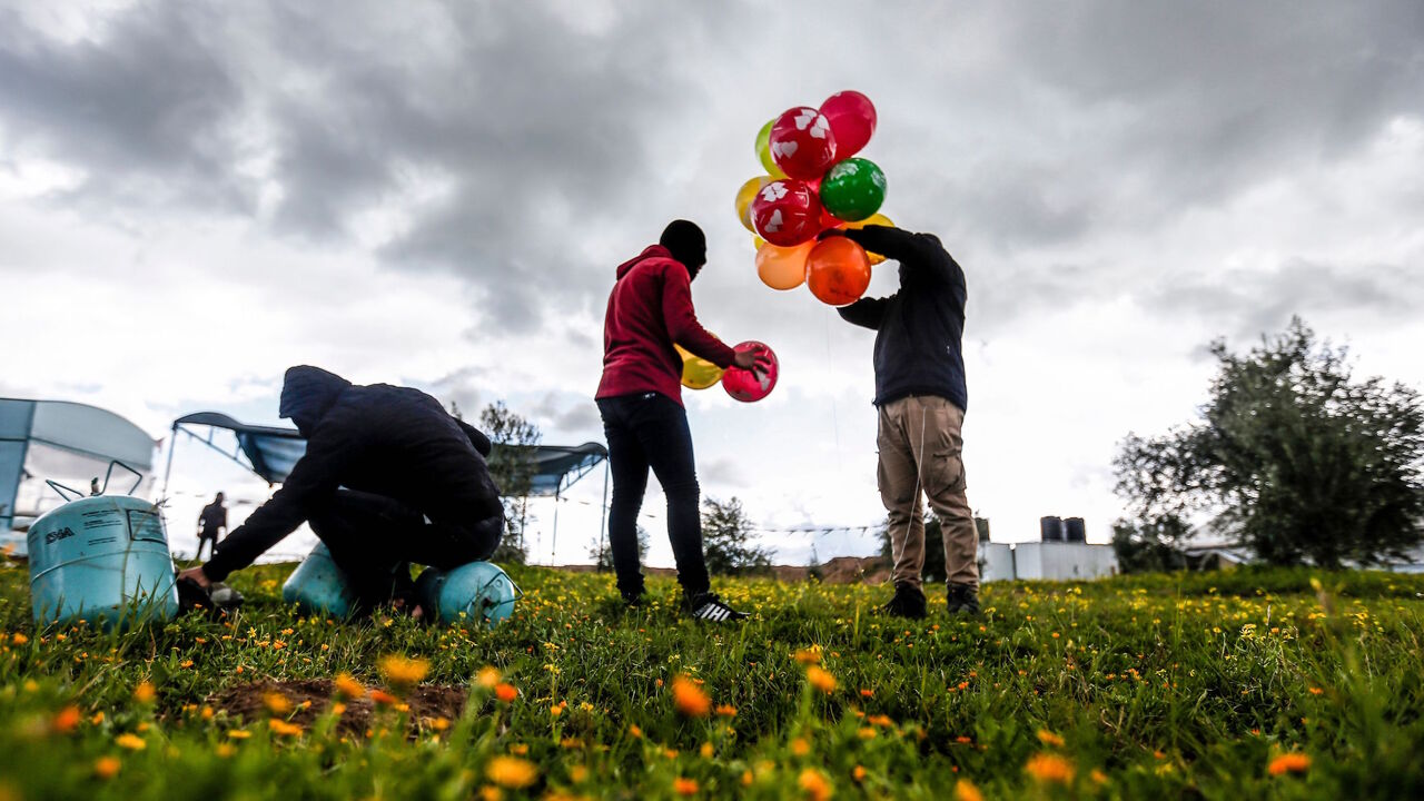 Masked Palestinians prepare to attach balloons to a gas canister before releasing it near Gaza's Bureij refugee camp, along the Israel-Gaza border fence, on February 10, 2020. (Photo by MAHMUD HAMS / AFP) (Photo by MAHMUD HAMS/AFP via Getty Images)