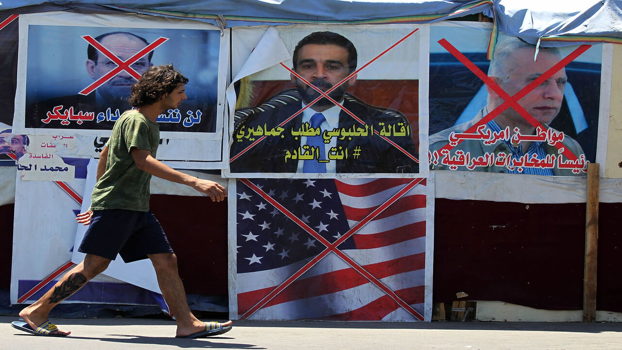 An Iraqi anti-government demonstrator walks past posters of Iraqi polititians and a US flag in Tahrir Square in the capital Baghdad, on August 1, 2020. - Iraq will hold its next parliamentary elections nearly a year early, the premier announced yesterday, as he seeks to make good on promises he offered when he came to power.
Protests began in October, with thousands taking to the streets of Baghdad and across the south.
Demonstrators demanded that the political system be dismantled, pointing to endemic corr