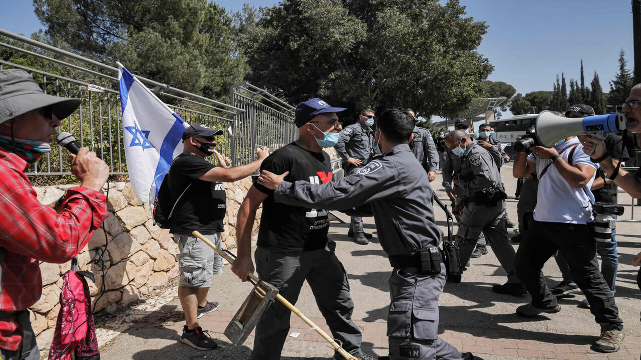 An Israeli policeman stands holding a demonstrator confronting him, all mask-clad due to the COVID-19 coronavirus pandemic, during a demonstration outside the Knesset (Israeli parliament) in Jerusalem on September 29, 2020, against a possible bill restricting protests amidst new pandemic regulations. - Israeli Health Minister Yuli Edelstein said on September 29 that there was "no way" the country's second nationwide coronavirus lockdown would be lifted after three weeks as originally planned. (Photo by Mena