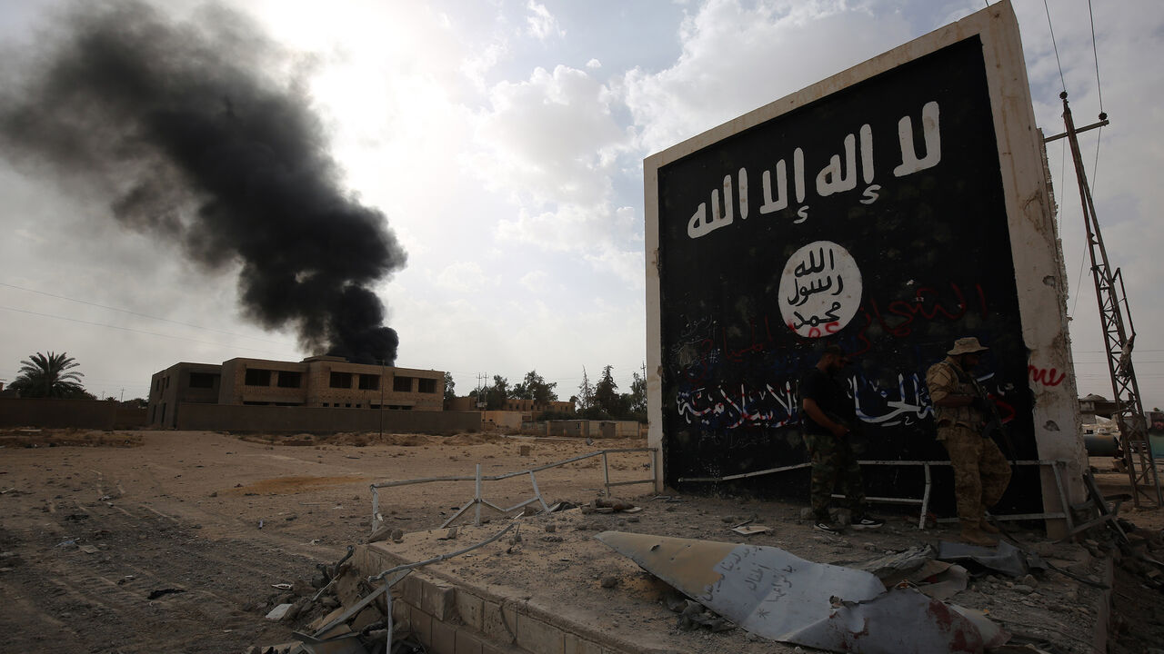 Iraqi fighters of the Hashed al-Shaabi (Popular Mobilisation units) stand next to a wall bearing the Islamic State (IS) group flag as they enter the city of al-Qaim, in Iraq's western Anbar province near the Syrian border as they fight against remnant pockets of Islamic State group jihadists on November 3, 2017.  / AFP PHOTO / AHMAD AL-RUBAYE        (Photo credit should read AHMAD AL-RUBAYE/AFP via Getty Images)