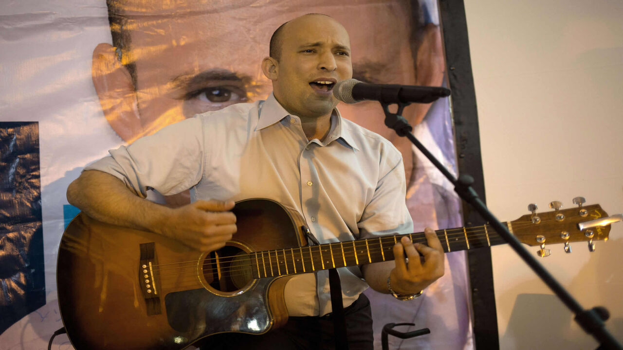 Israeli Economy Minister and head of the right-wing Jewish Home party, Naftali Bennett plays the guitar and sings during an election campaign gathering for the Jewish community in Kibbutz Kfar Etzion in the Gush Etzion settlement block in the West Bank, on March 12, 2015, ahead of a snap general election scheduled March 17. Bennett, 42, is a champion of the settler movement and a key challenger of Netanyahu to head Israel's rightwing. AFP PHOTO / MENAHEM KAHANA        (Photo credit should read MENAHEM KAHAN