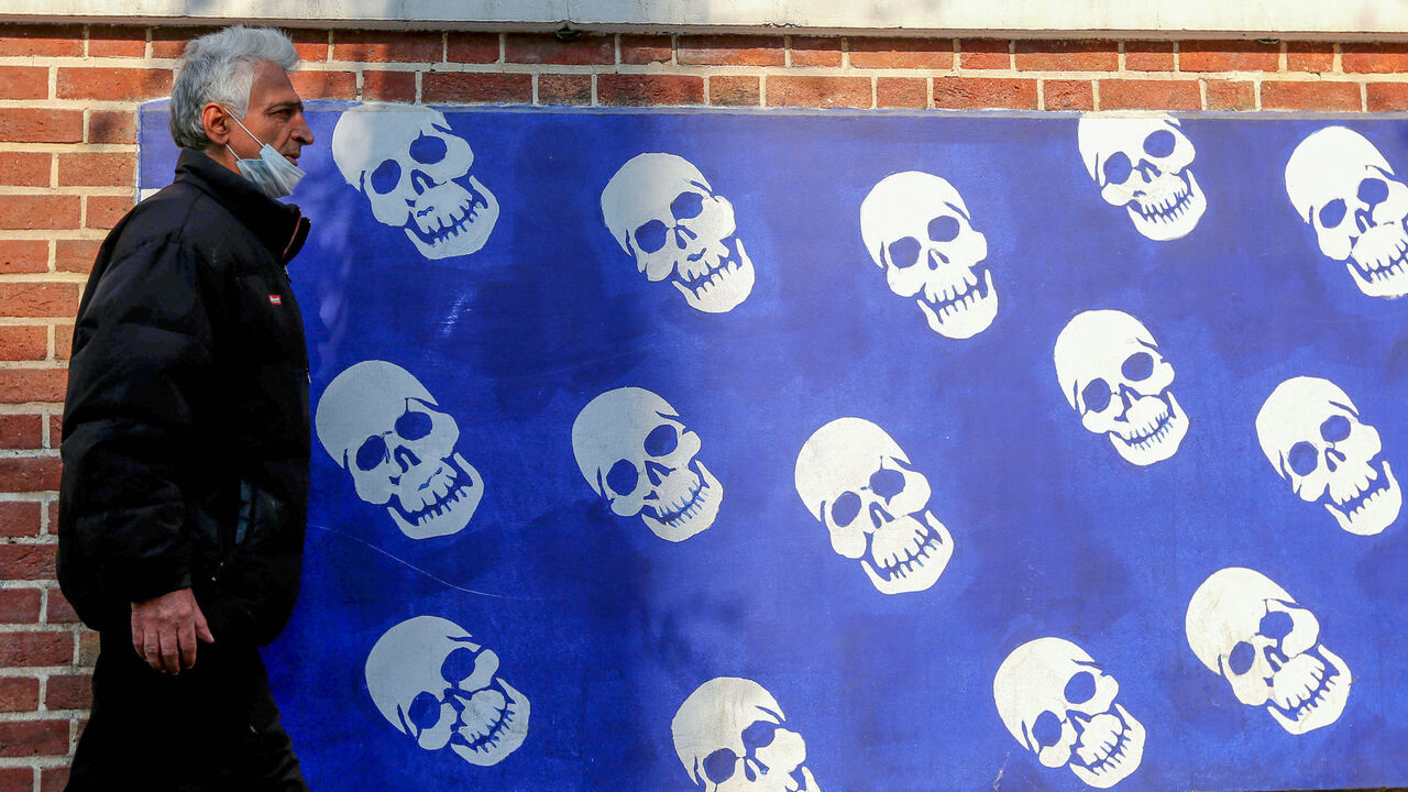 An Iranian man wearing a protective mask amid the COVID-19 pandemic, walks past a mural painted on the outer walls of the former US embassy in the capital Tehran, on December 30, 2020. (Photo by ATTA KENARE / AFP) (Photo by ATTA KENARE/AFP via Getty Images)