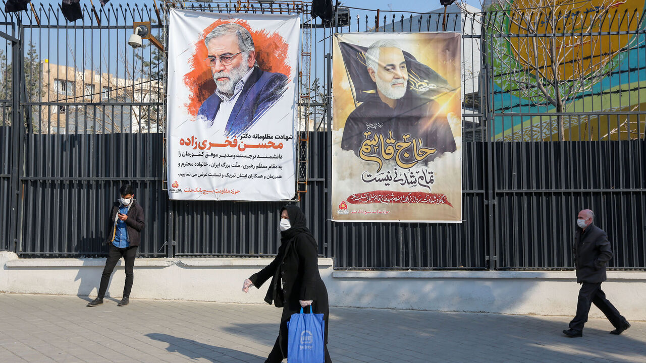 Iranians walk past a poster depicting late Revolutionary Guards commander Qasem Soleimani (R) and nuclear scientist Mohsen Fakhrizadeh, assassinated last month, in the capital Tehran, on December 30, 2020. - On January 3, Iraq will mark a year since a US drone strike killed Soleimani, head of the elite external operations of Iran's Revolutionary Guards, alongside Abu Mahdi al-Muhandis, the deputy head of Iraq's powerful Tehran-aligned Hashed Al-Shaabi paramilitary network, nearly sparking a conflict that ma