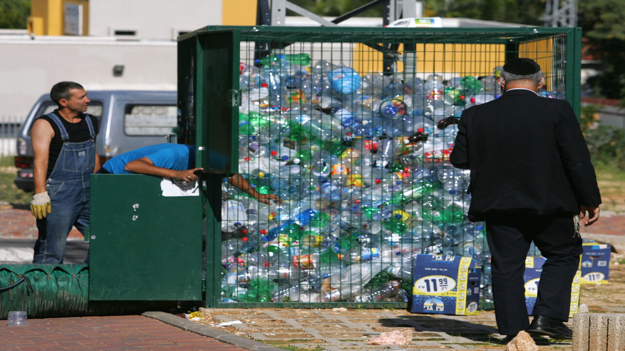 ROSH HA'AYIN, ISRAEL - NOVEMBER 21: A passing ultra-Orthodox Jew watches as Aviv Recycling workers use a strong vacuum to move plastic bottles from a collection cage into their truck November 21, 2006 in Rosh Ha'Ayin in central Israel. Aviv managers say they recycle about 15 percent of the country's PET plastic waste annually, some 4,000 metric tons or 80 million bottles, but have the capacity to sort, clean, crush and sell more than double that if recycling programs in Israel were more efficient.  (Photo b