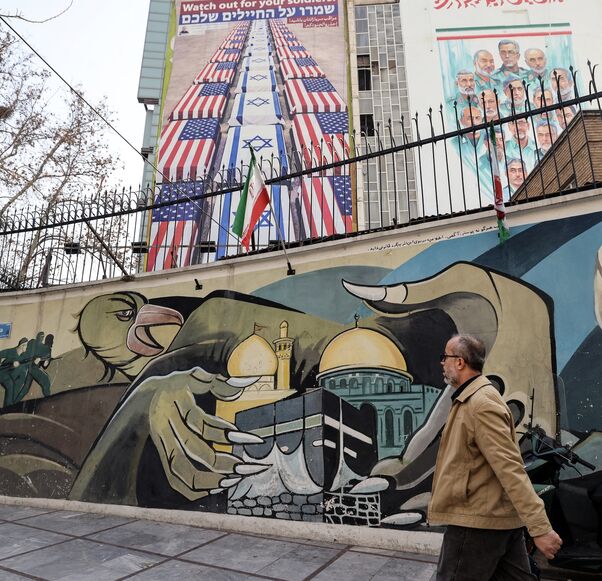 An Iranian man walks past an anti-US and anti-Israel banner hanging on a building in Palestine Square in Tehran on Jan. 27, 2026.