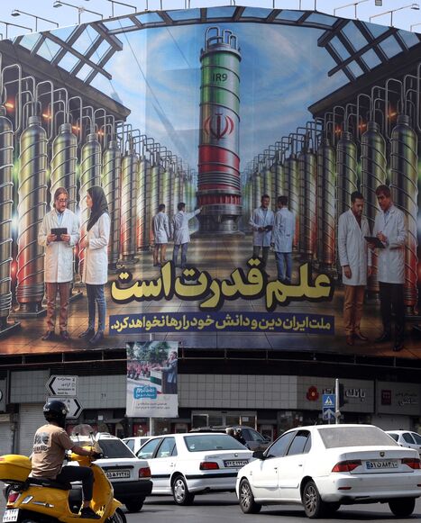 Iranians drive next to a billboard displaying pictures of nuclear scientists, centrifuges and a sentence reading in Farsi "Science is the power," at Enqelab Square in Tehran, on Aug. 29, 2025. 