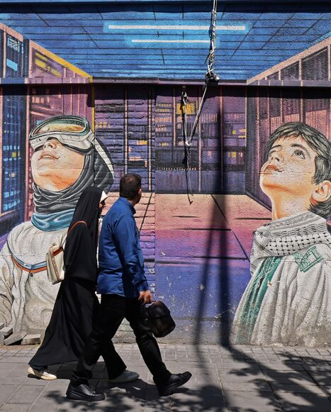 People walk past a wall mural along the roadside in Tehran on April 12, 2026.